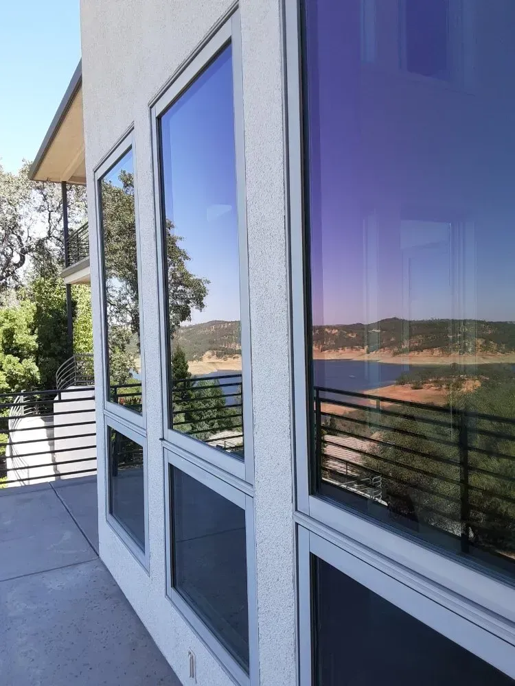 Three large windows with tinted glass reflecting a landscape and a building's exterior.