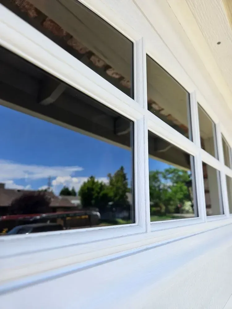 White-framed windows reflecting a blue sky with clouds and trees.