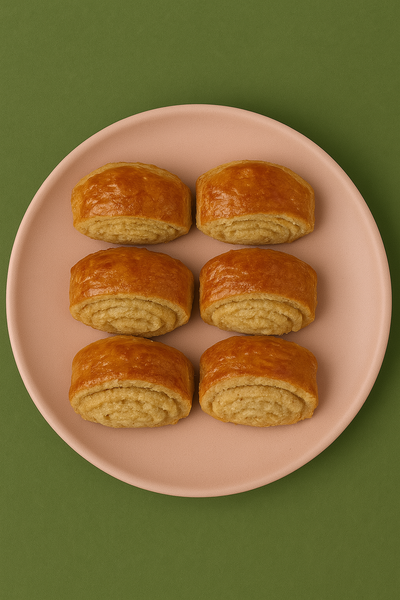 Six golden, baked kyata pastries arranged on a pink plate against a green background.