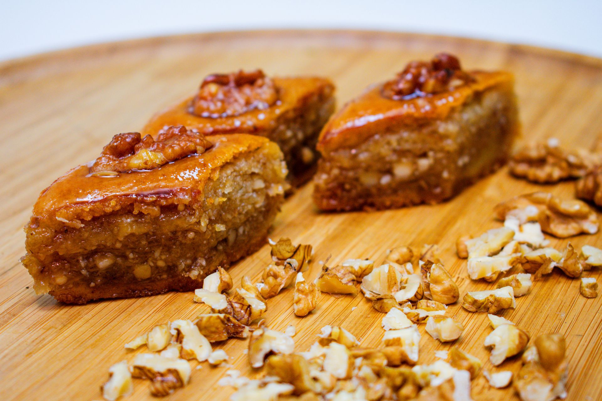 Three pieces of pakhlavawith walnuts on a wooden serving board, scattered walnut pieces nearby.