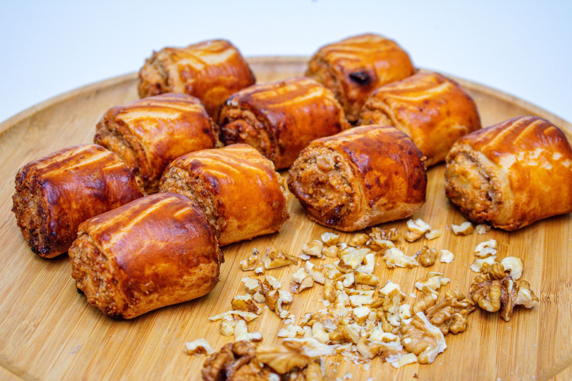 Golden baked pastry rolls with walnut filling on a wooden plate, surrounded by chopped walnuts.