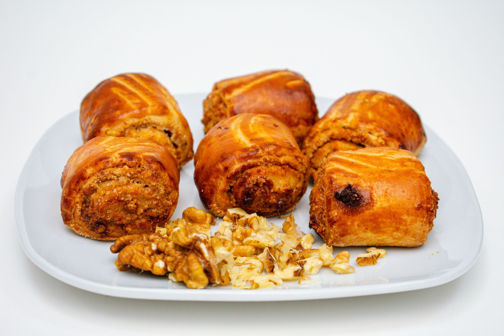 Six golden-brown pastries on a white plate with a side of chopped walnuts.