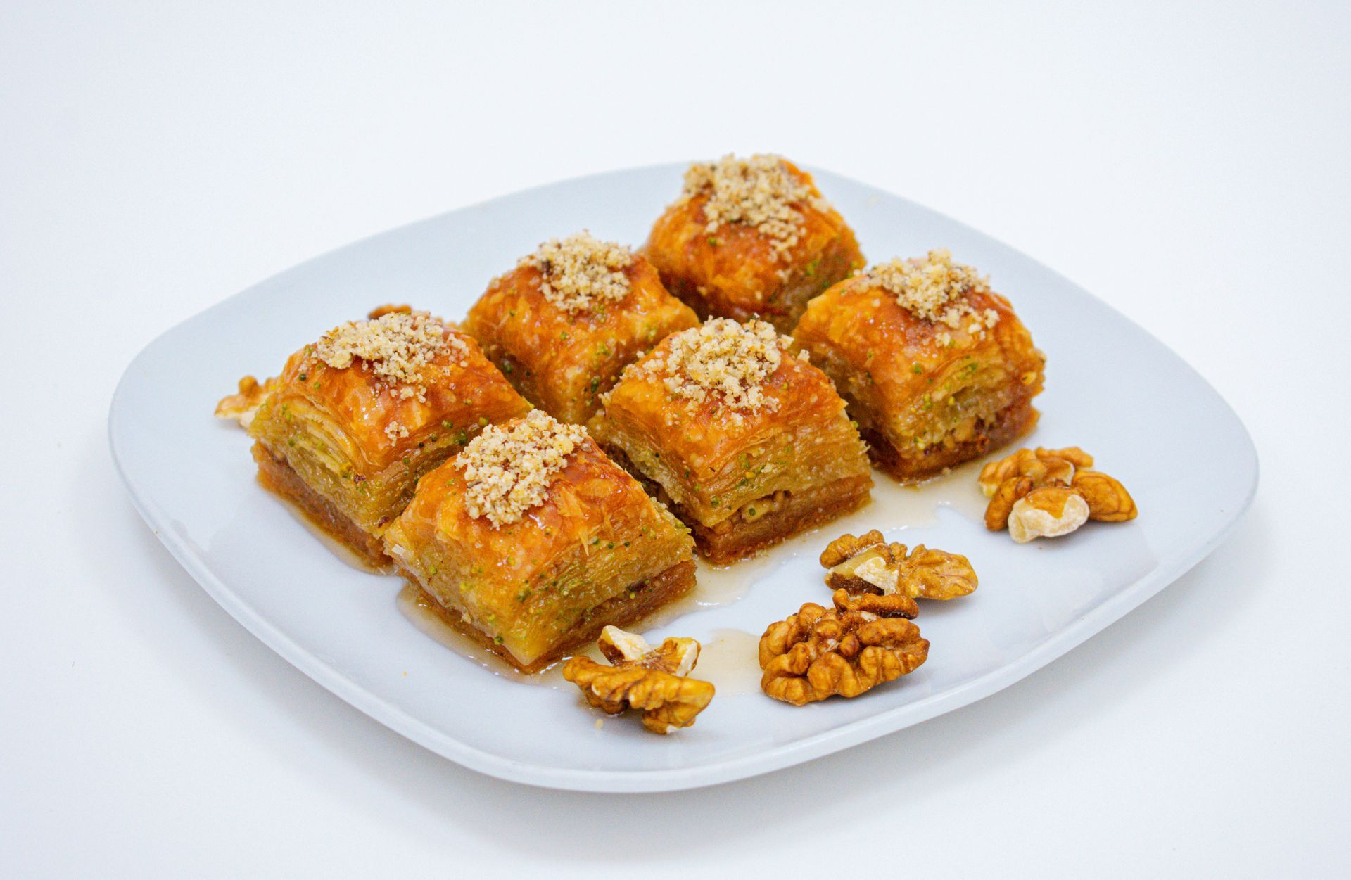 Baklava pastries on a white square plate, topped with walnuts.