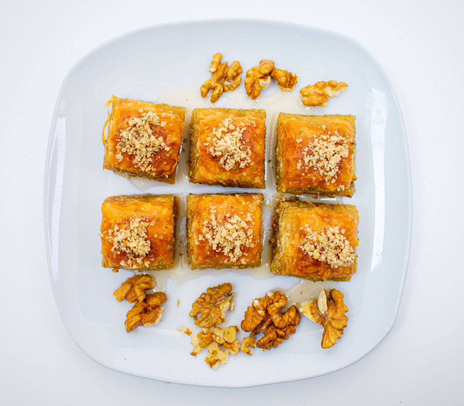 Baklava squares on a white plate, topped with walnuts.