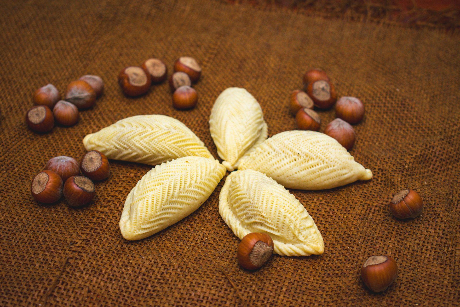 Hazelnut pastries arranged in a flower shape with hazelnuts on a brown textile surface.