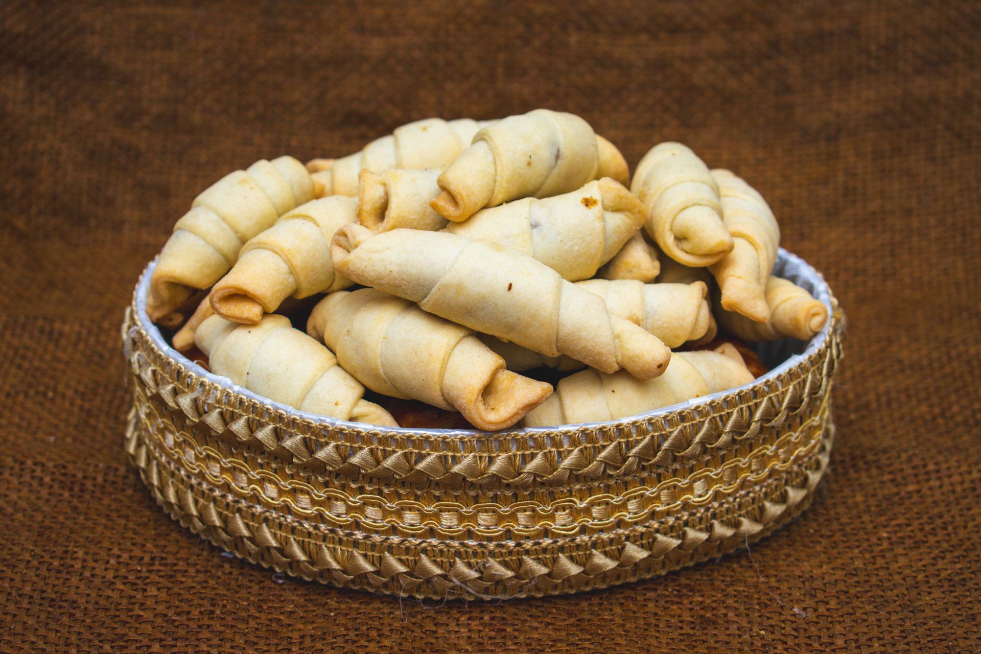 Basket of golden, crescent-shaped cookies on a brown textured surface.
