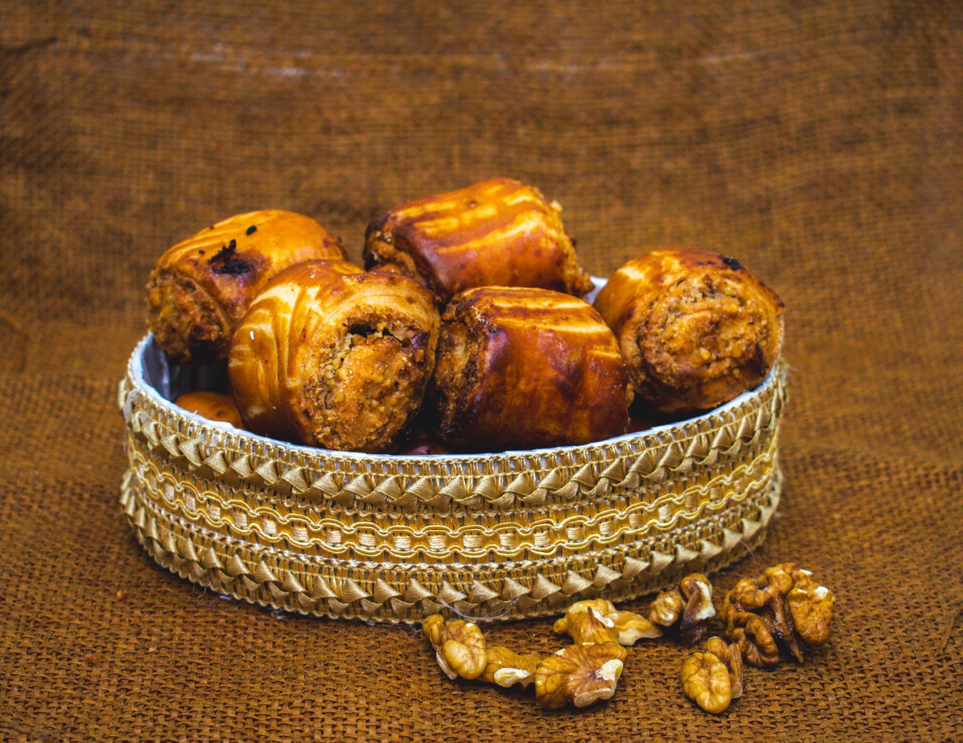 Baked pastries in a woven basket with scattered walnuts on a brown cloth background.