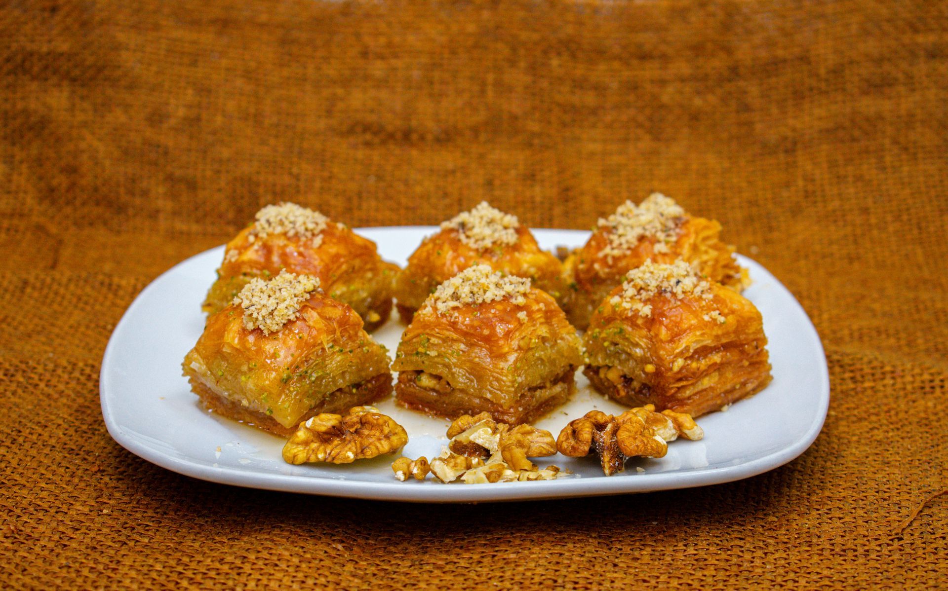 Baklava pastries on a white plate, garnished with walnuts, set against a brown background.