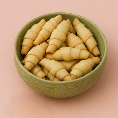 Bowl of golden-baked, crescent-shaped cookies. Green bowl on pink background.