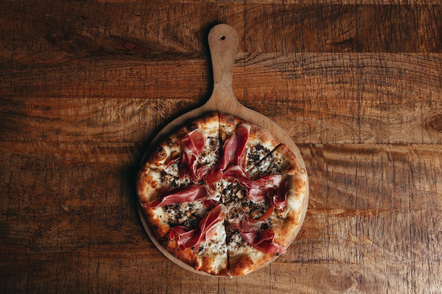 A pizza is sitting on a wooden cutting board on a wooden table.