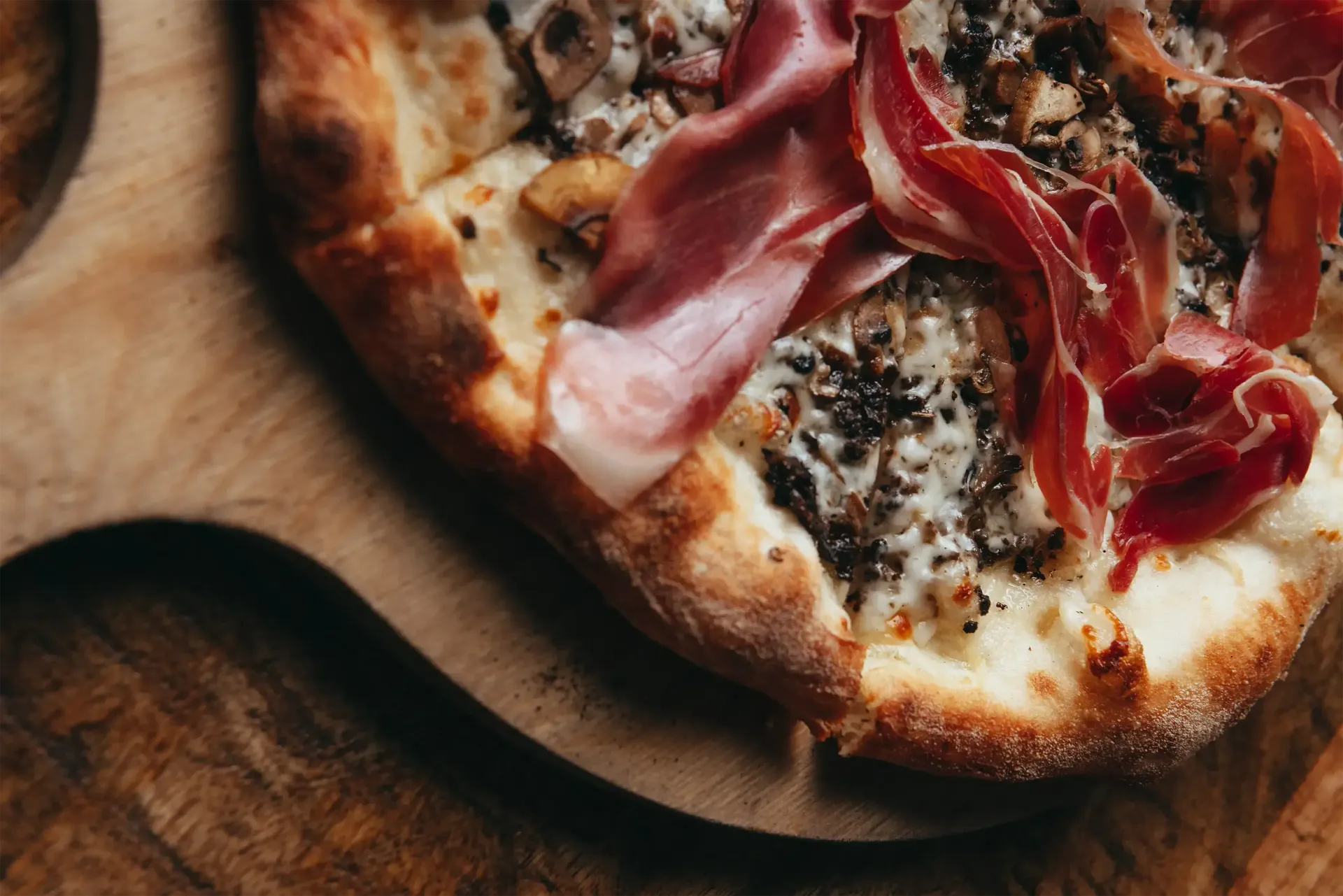 A pizza with ham , mushrooms and cheese on a wooden cutting board.