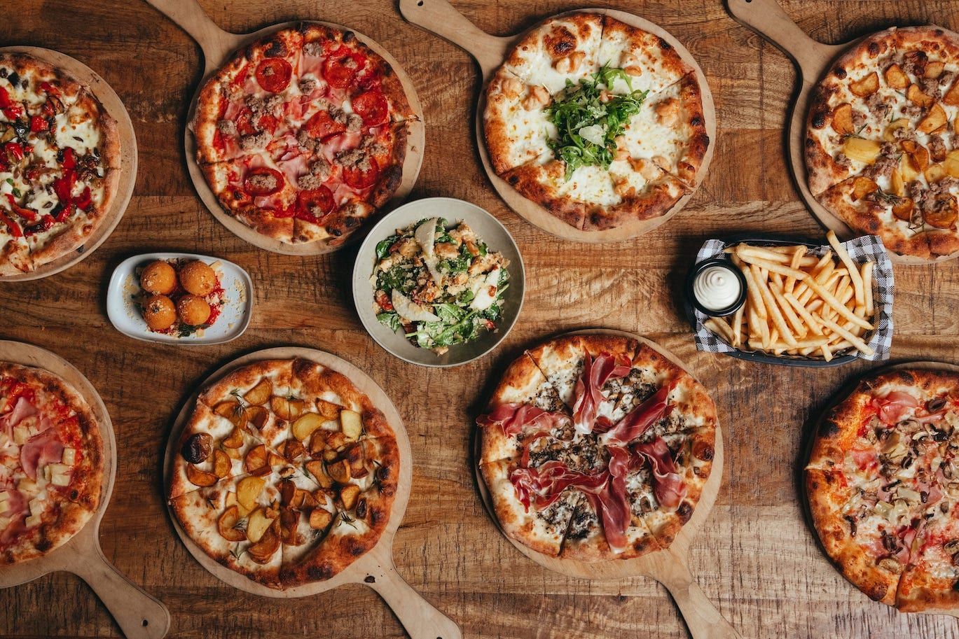 A wooden table topped with a variety of pizzas and french fries.