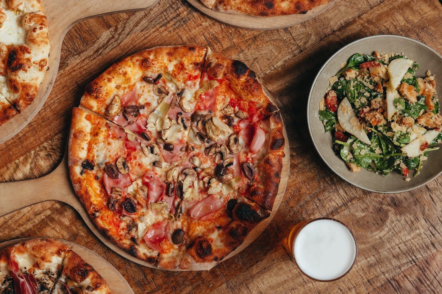 A pizza and a salad are on a wooden table.