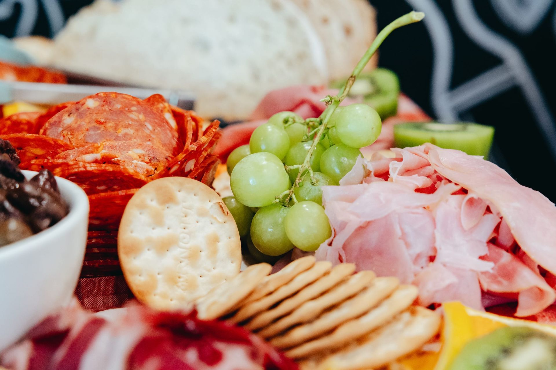 A close up of a plate of food with crackers , grapes , ham and cheese.