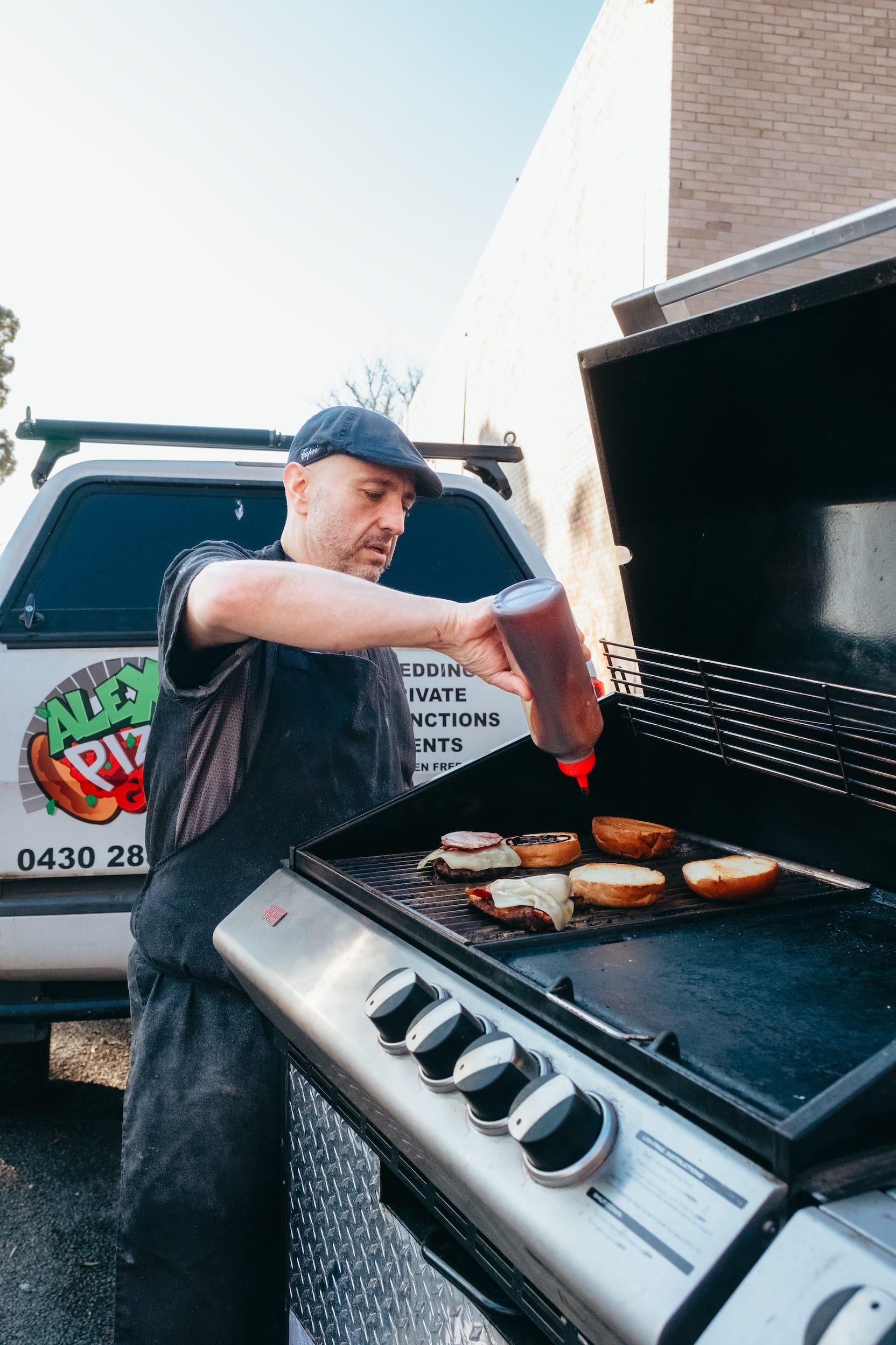 A man is cooking food on a grill in front of a truck.