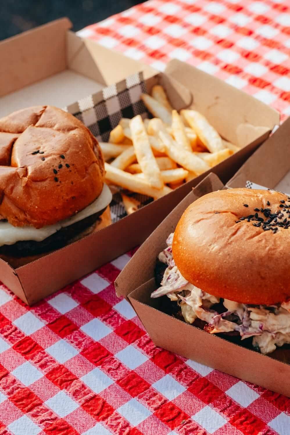 Two hamburgers and french fries in cardboard boxes on a checkered table cloth.