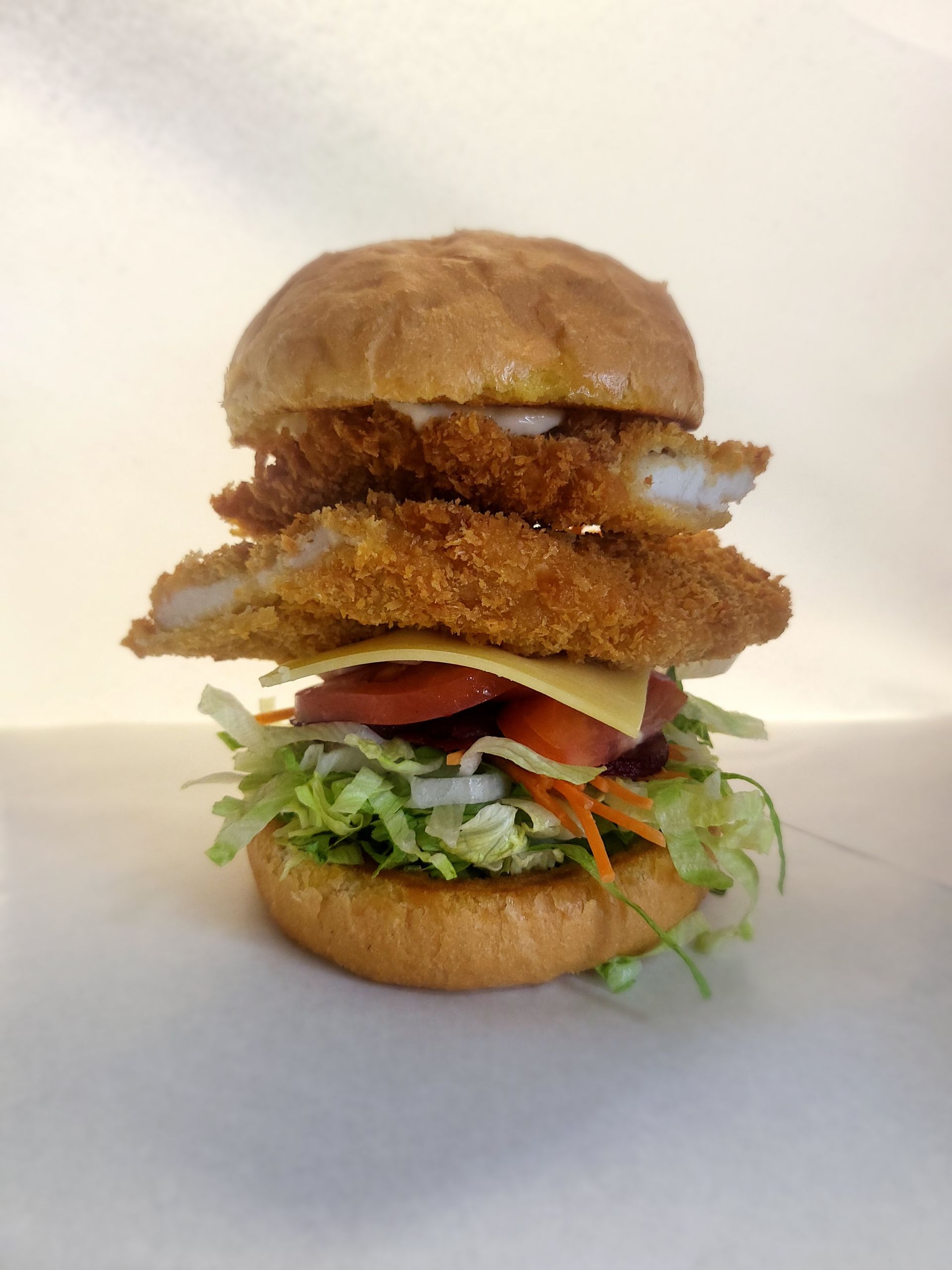 Fish sandwich with lettuce, tomato, cheese, and two fried fish fillets on a bun.