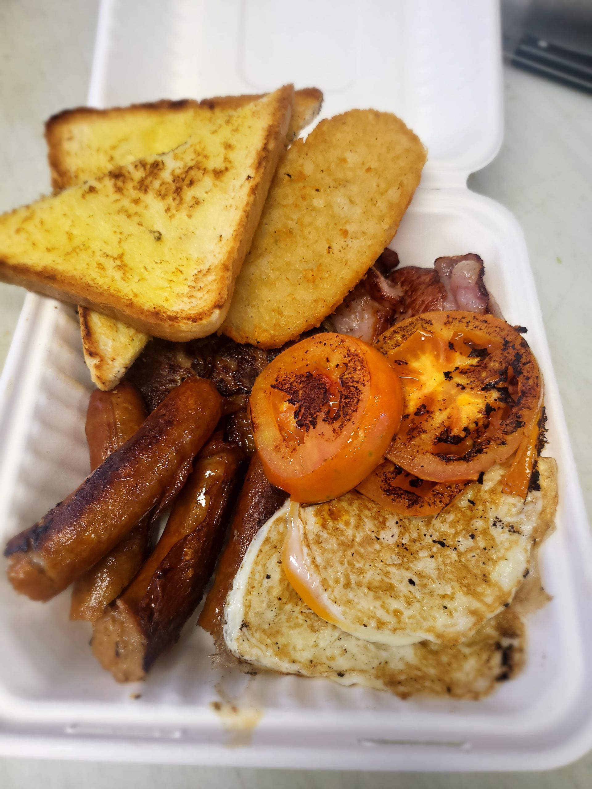 Breakfast meal in a white container: toast, hash brown, bacon, tomato, egg, and sausages. — Boundary Street Fish & Burger Bar in Railway Estate, QLD