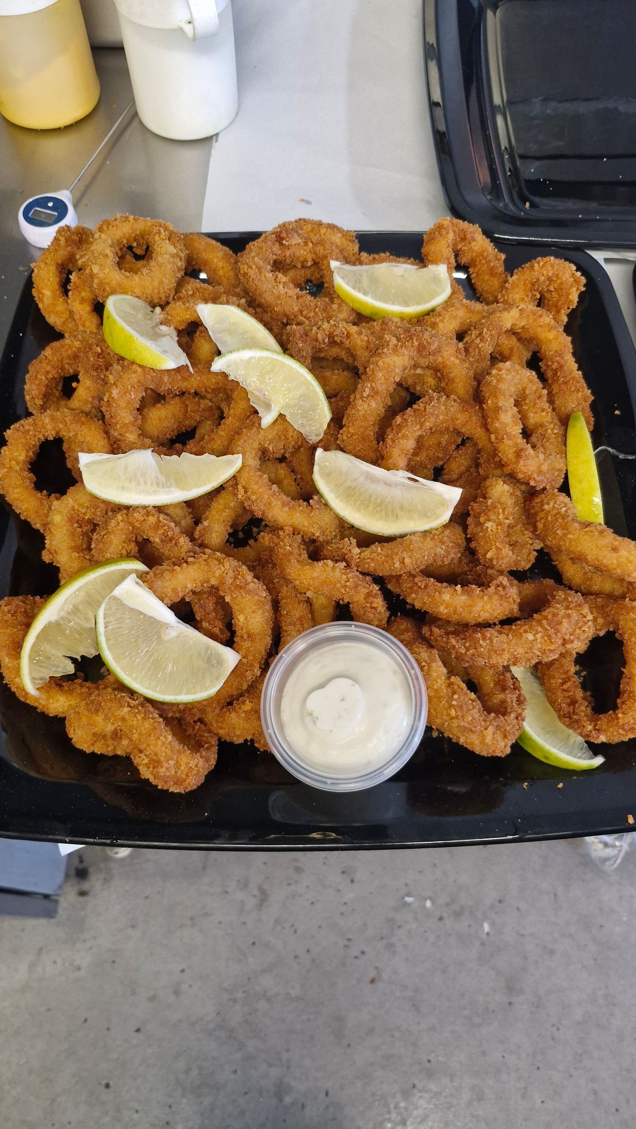Fried calamari rings on a black plate with lime wedges and dipping sauce. — Boundary Street Fish & Burger Bar in Railway Estate, QLD