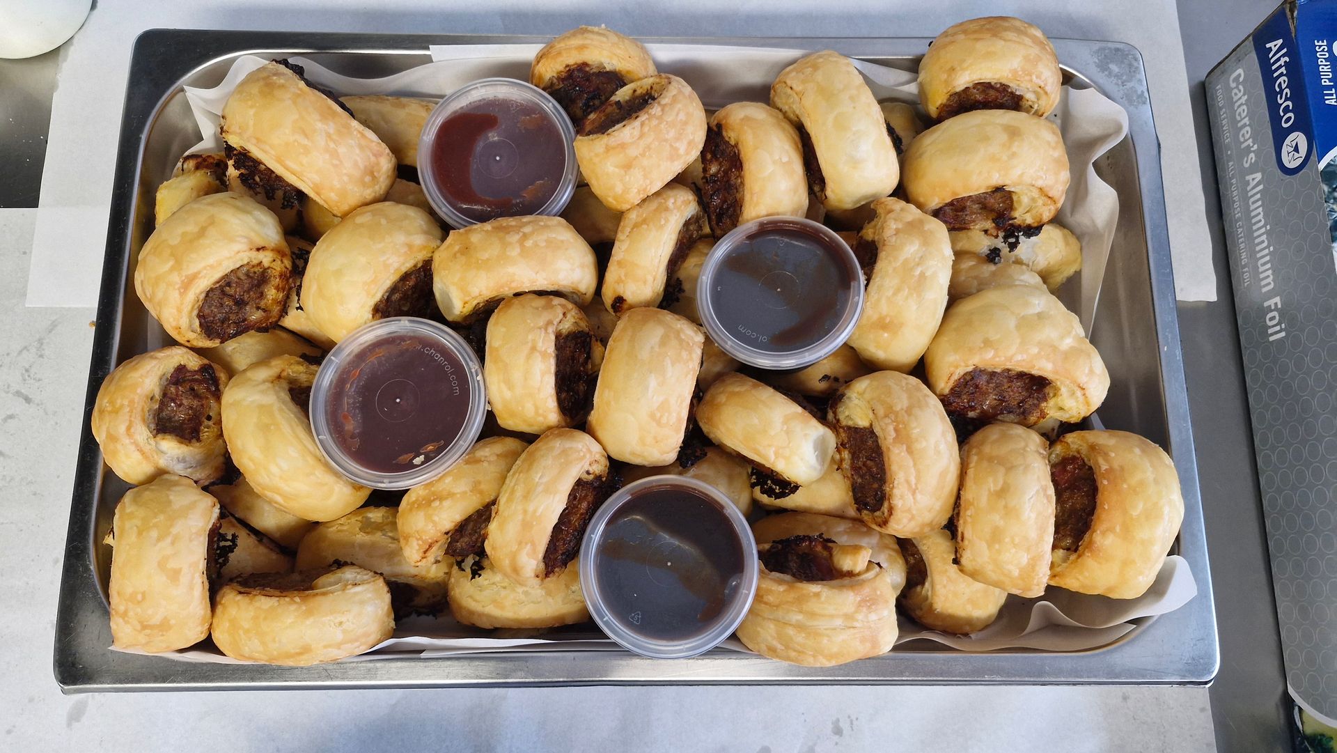 Sausage rolls and small sauce cups on a metal tray. — Boundary Street Fish & Burger Bar in Railway Estate, QLD