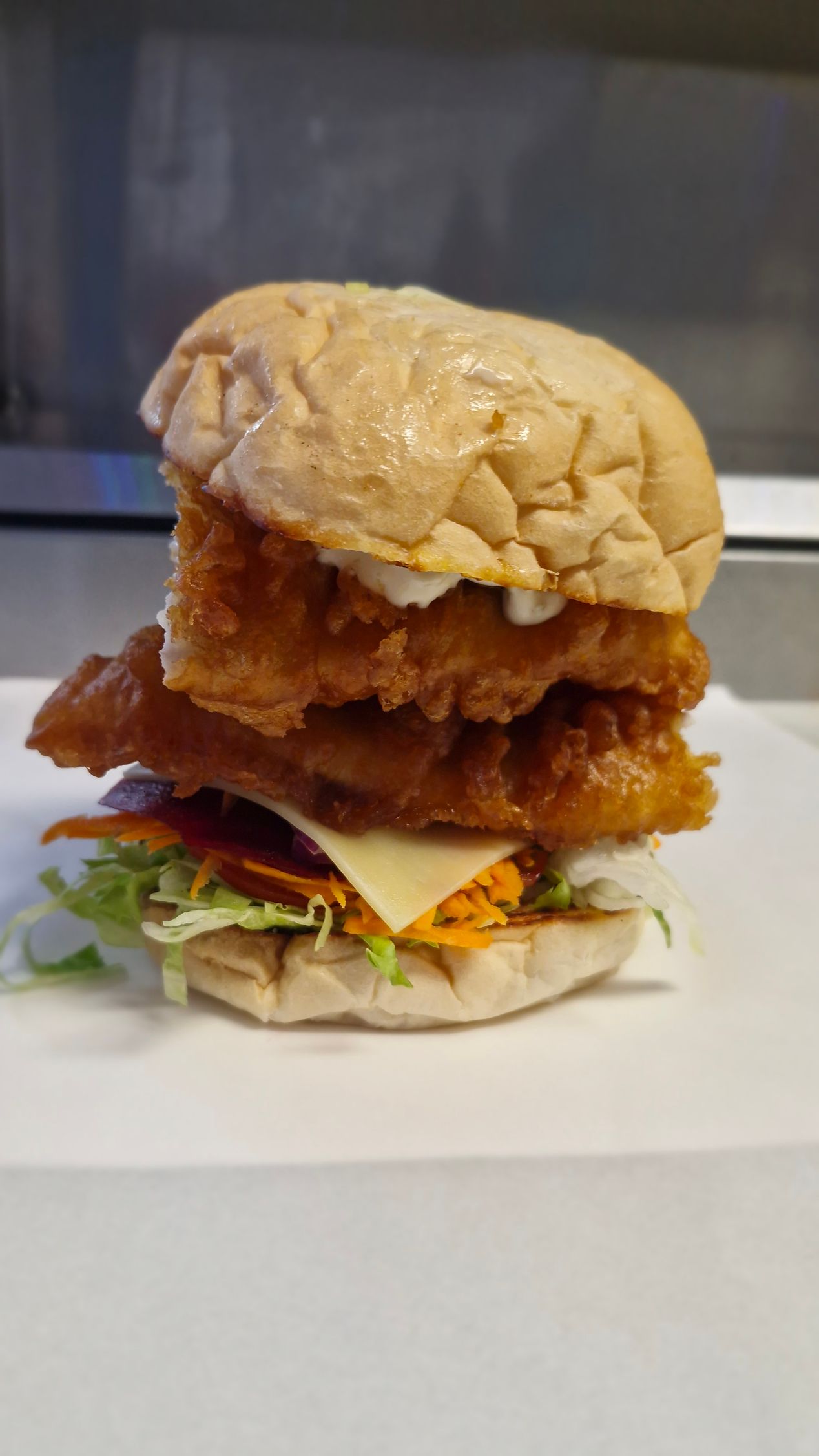 Double-decker fish burger with a crispy, golden fried patty, cheese, and lettuce on a bun. — Boundary Street Fish & Burger Bar in Railway Estate, QLD