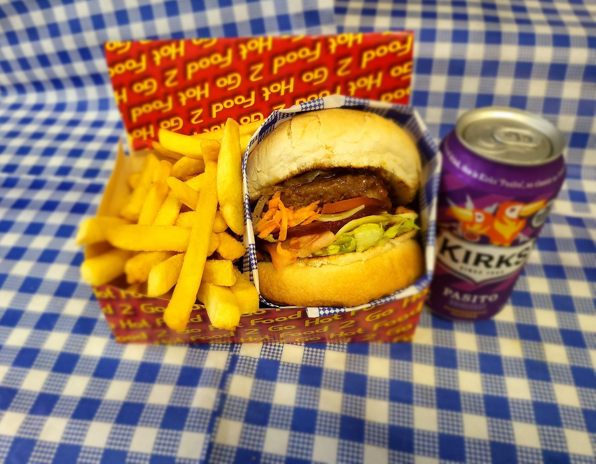 Hamburger with fries and a drink on a blue checkered tablecloth.