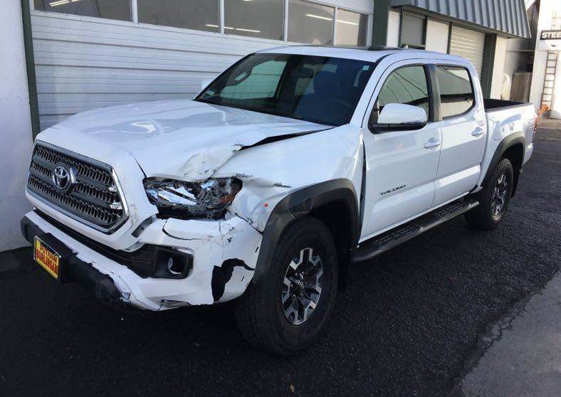 White Toyota Tacoma pickup truck with front-end damage parked outside a building.