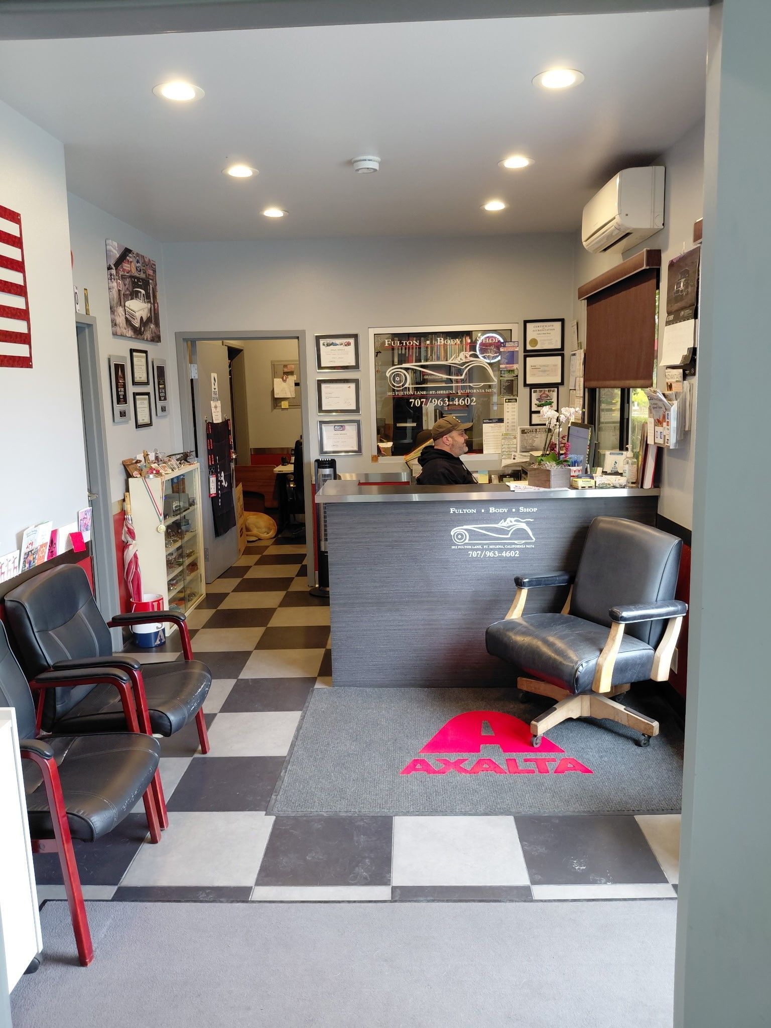 Interior of a shop with a reception desk, chairs, and an American flag. A person sits at the desk.