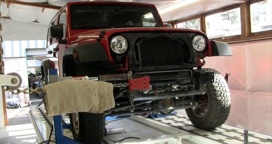 Red Jeep Wrangler in a repair shop, front end disassembled, raised on a lift.
