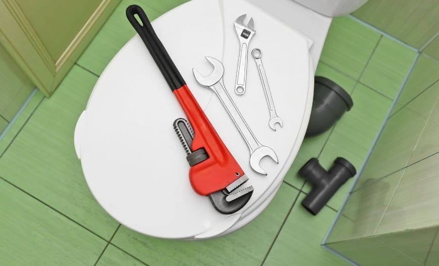 A toilet with a wrench and other tools on it