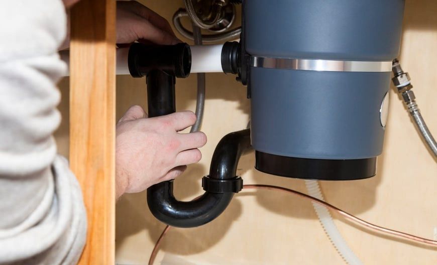 A person is fixing a garbage disposal under a sink.