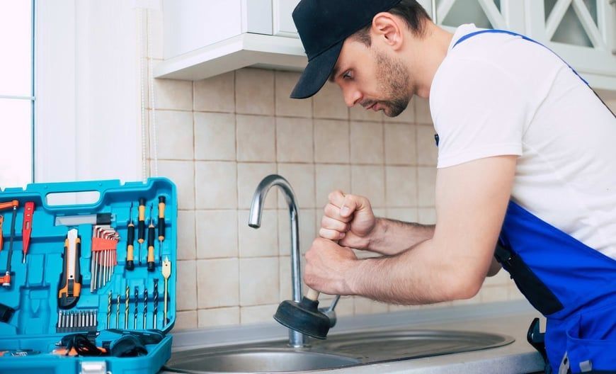 A man is fixing a sink with a plunger in a kitchen.