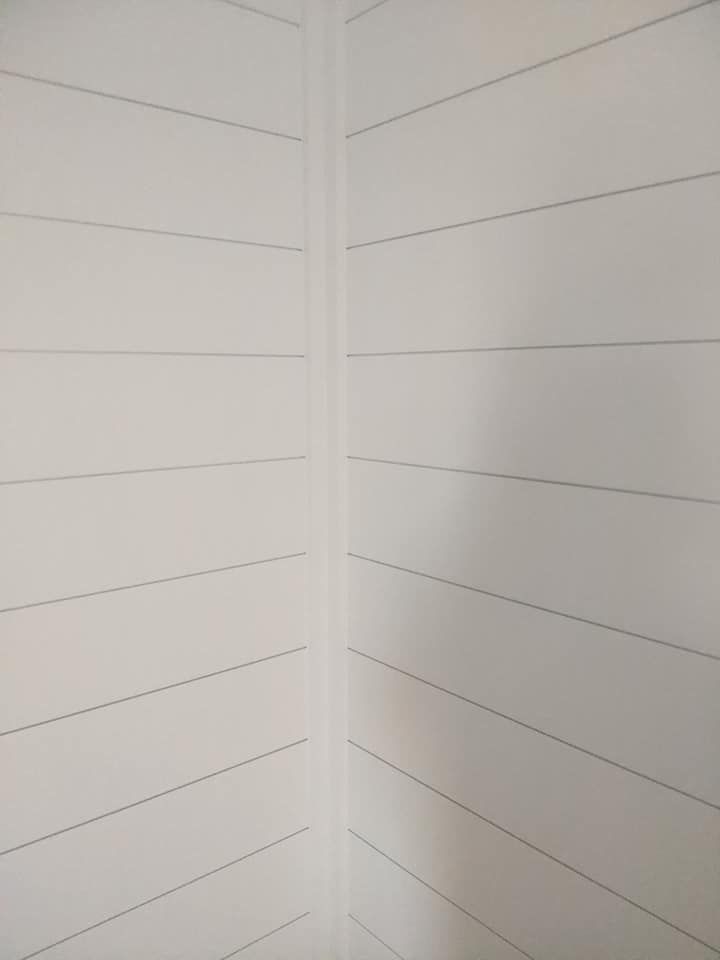 A corner of a room with white wood paneling on the walls.