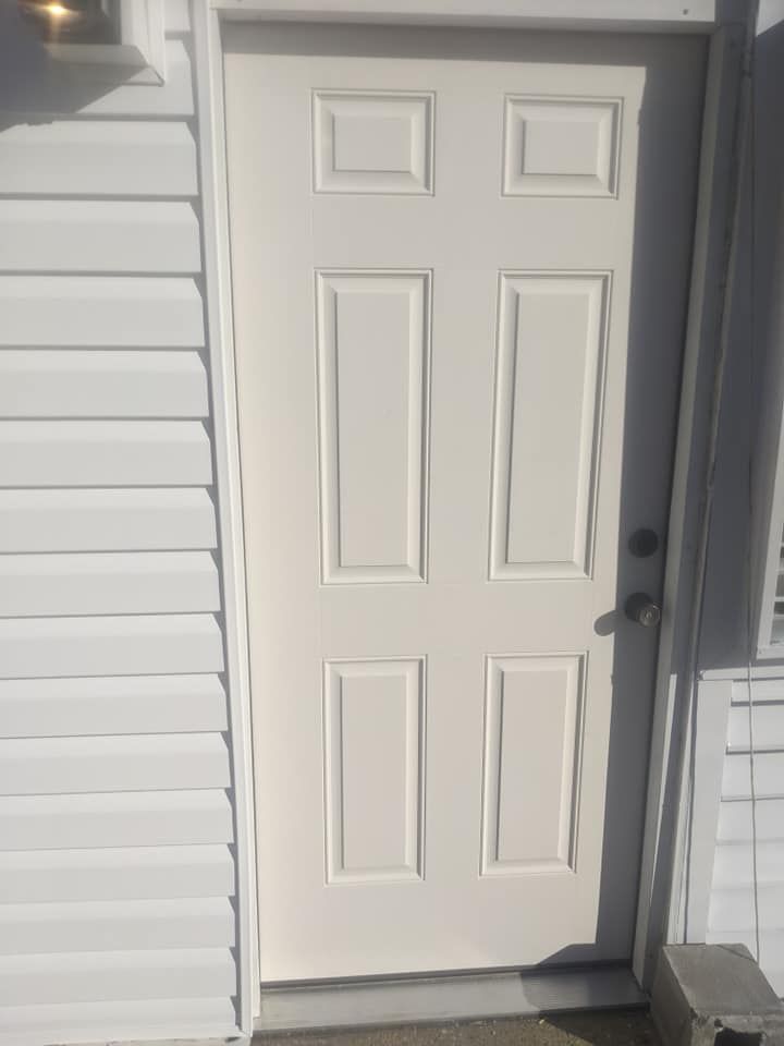 A white door is sitting on the side of a white house.