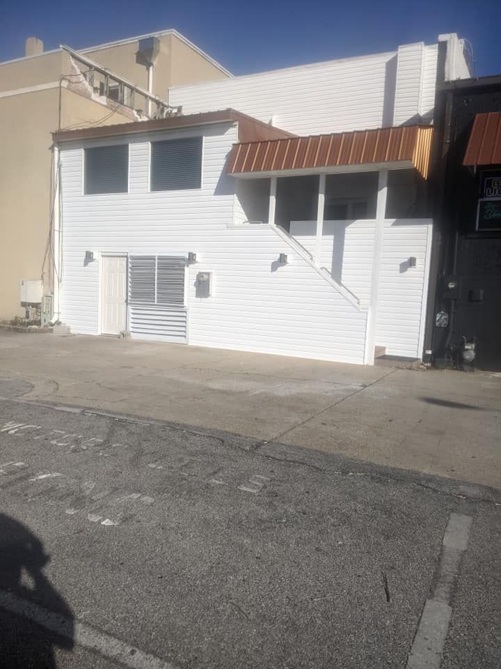 A white building with stairs leading up to it is next to a parking lot.