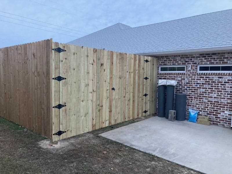 A wooden fence is sitting in front of a brick house.