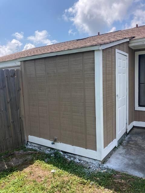 A brown shed with a white door is in the backyard of a house.
