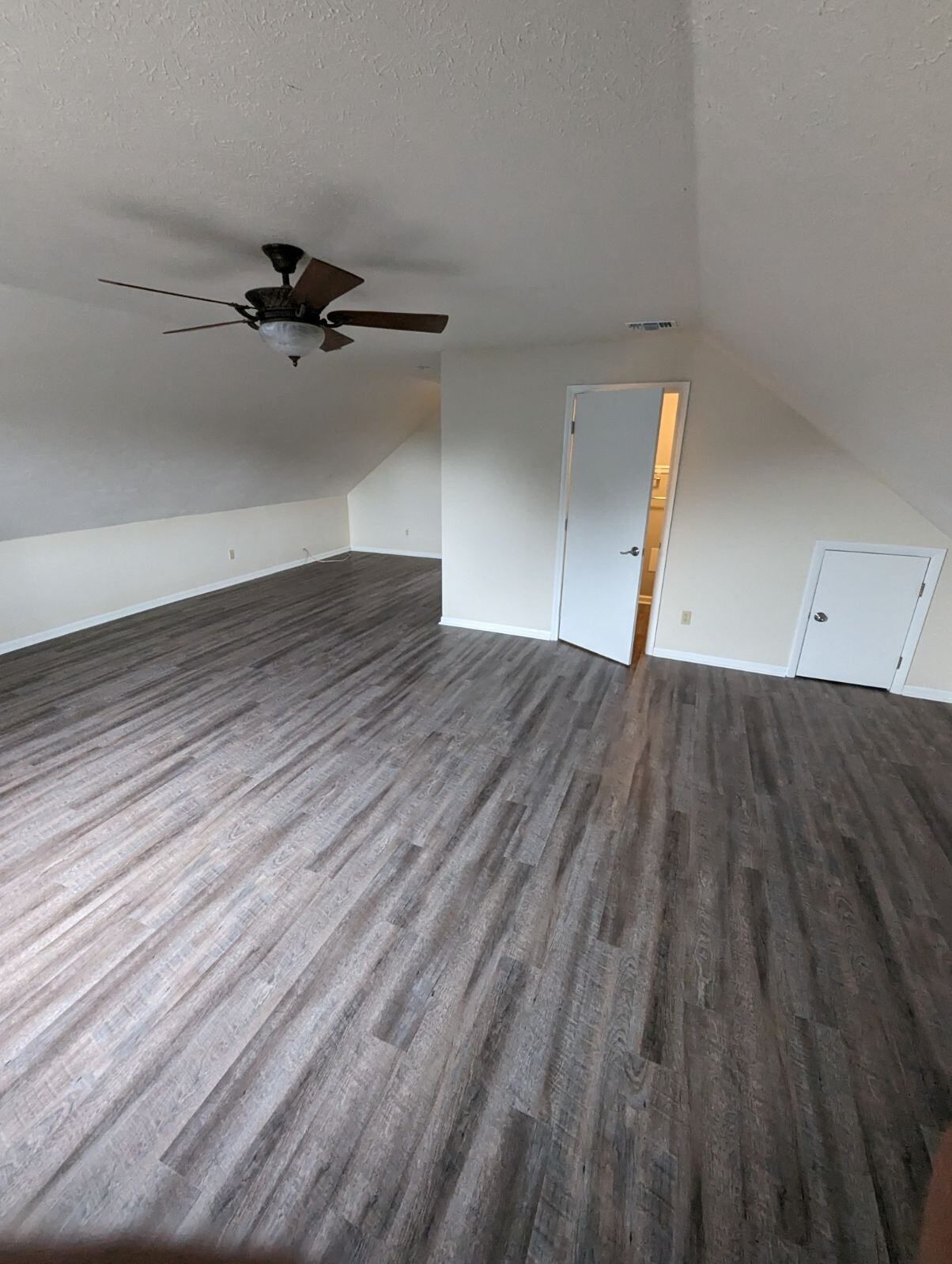 An empty room with hardwood floors and a ceiling fan.