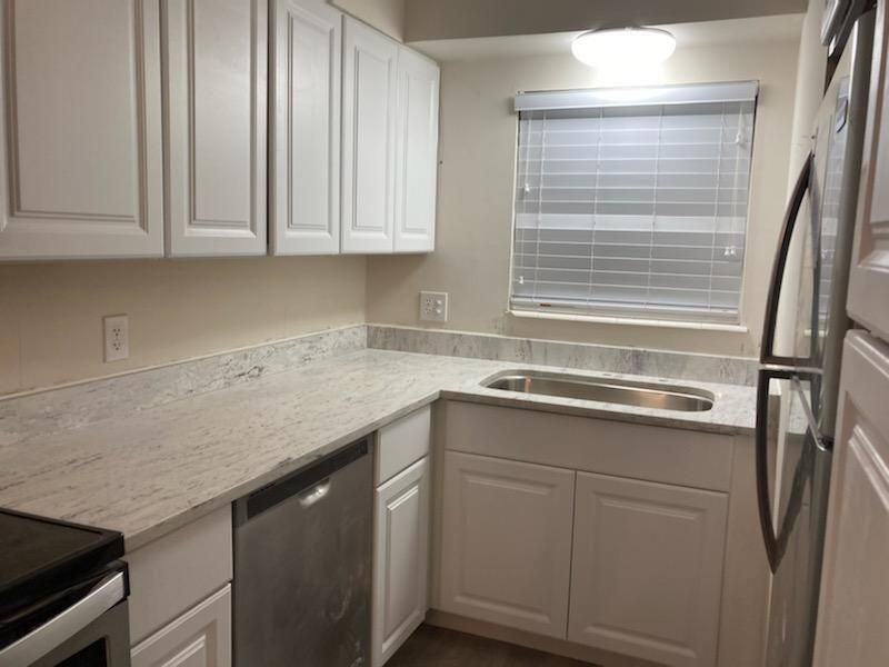 A kitchen with white cabinets , stainless steel appliances , a sink and a window.
