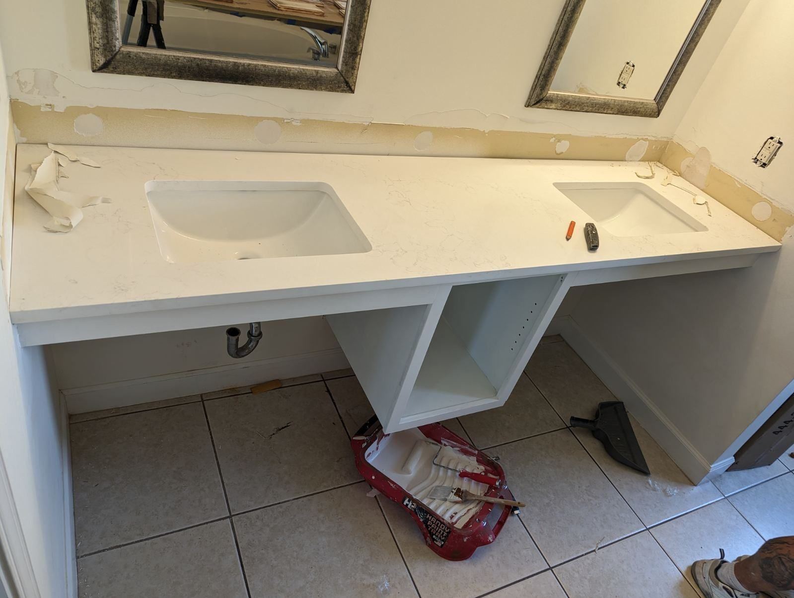A bathroom with two sinks and a paint roller on the floor