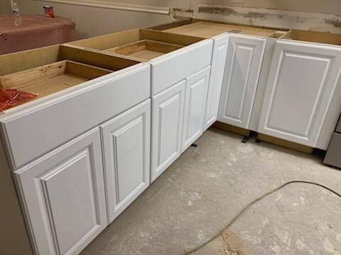A kitchen under construction with white cabinets and wooden counter tops.