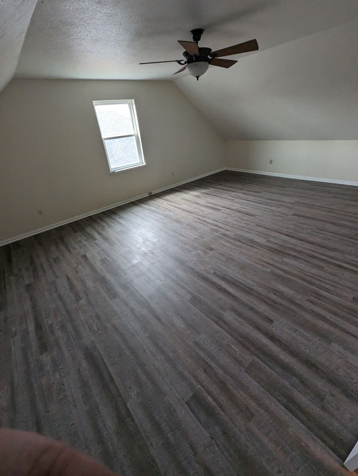 A large empty room with a ceiling fan and a window.