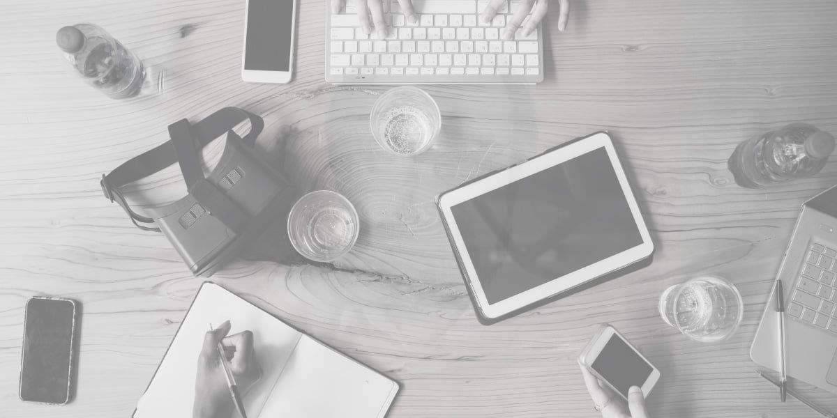 Uma foto em preto e branco de uma mesa com um laptop, tablet, celular e notebook.