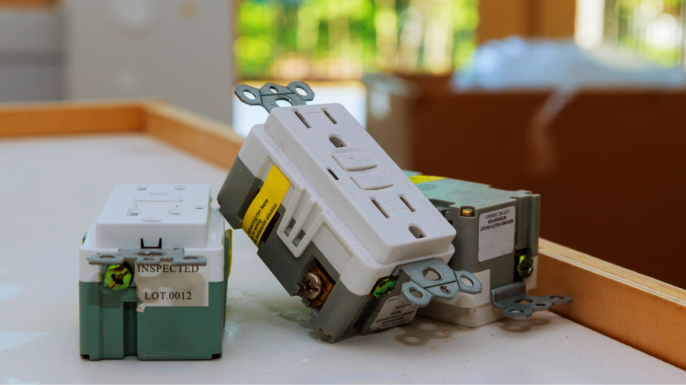 Three electrical outlets, including a GFCI outlet, resting on a white surface with a blurred background.