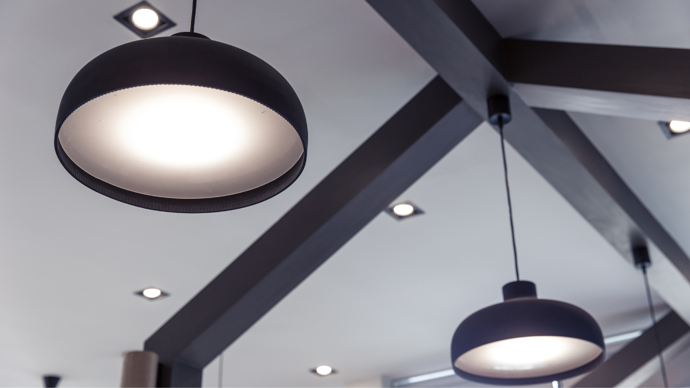 Two dark pendant lights hang from a white ceiling with exposed wooden beams and recessed lights.