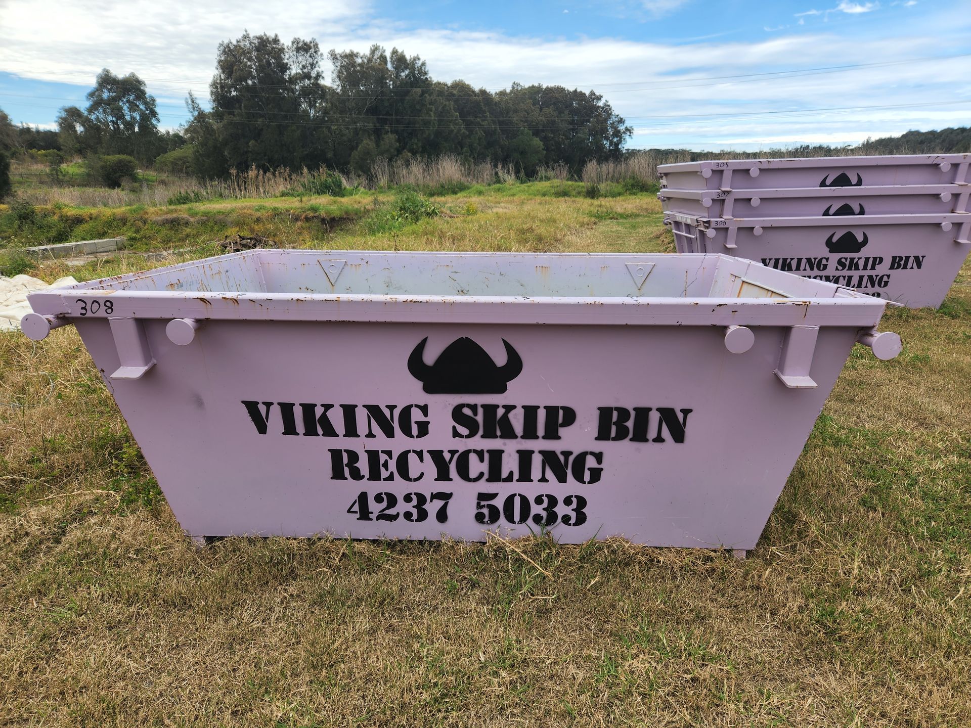 A Purple skip bin on grass with a stack of skip bins in the distance — Viking Skip Bin Recycling In Dunmore, NSW