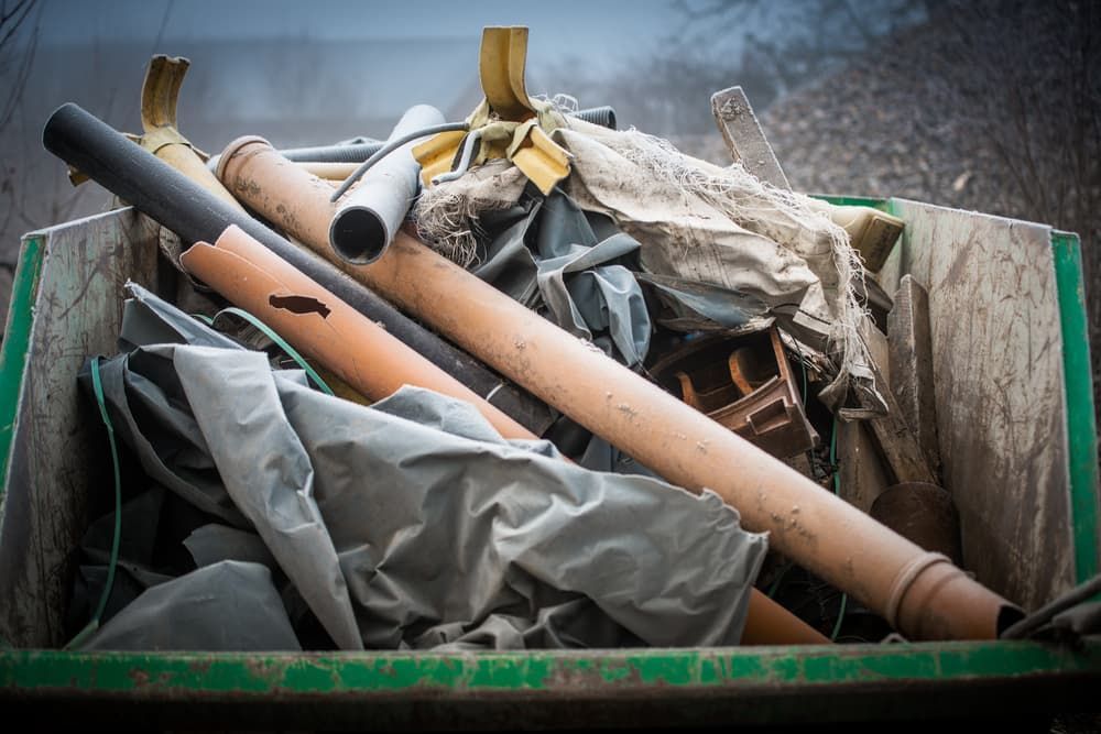 A Green Bin Filled With a Bunch of Junk Including Pipes — Viking Skip Bin Recycling In Dapto, NSW