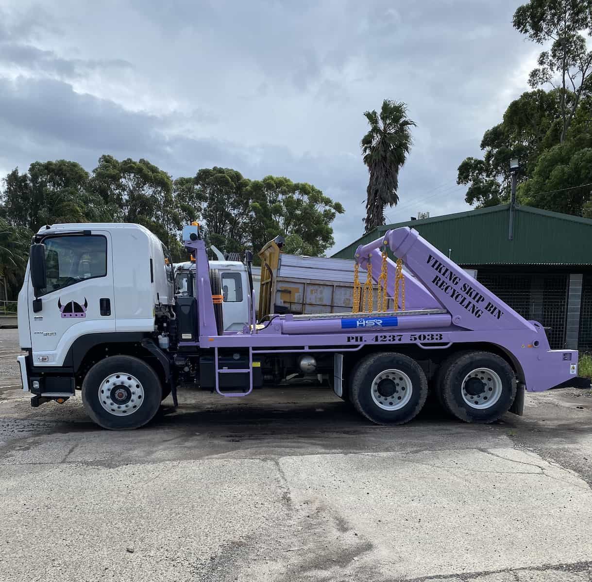 A Light Purple Hook Lift Truck Parked On Pavement In Front Of Trees — Viking Skip Bin Recycling In Dunmore, NSW