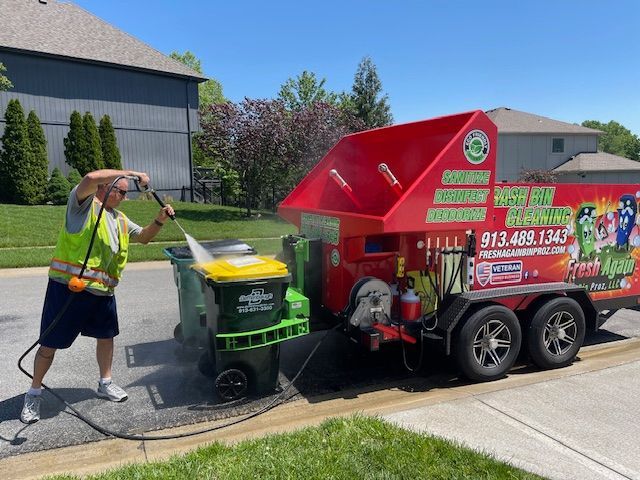 A man is cleaning a trash can next to a trash truck