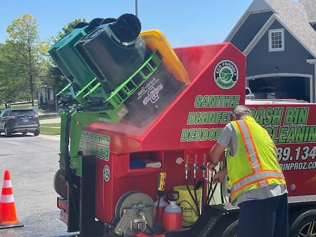 A man in a yellow vest is working on a trash bin cleaning machine